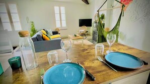 Una mesa de comedor dispuesta con platos azules, copas de vino y cubiertos en una sala de estar moderna con un sofá, una hamaca y una chimenea.