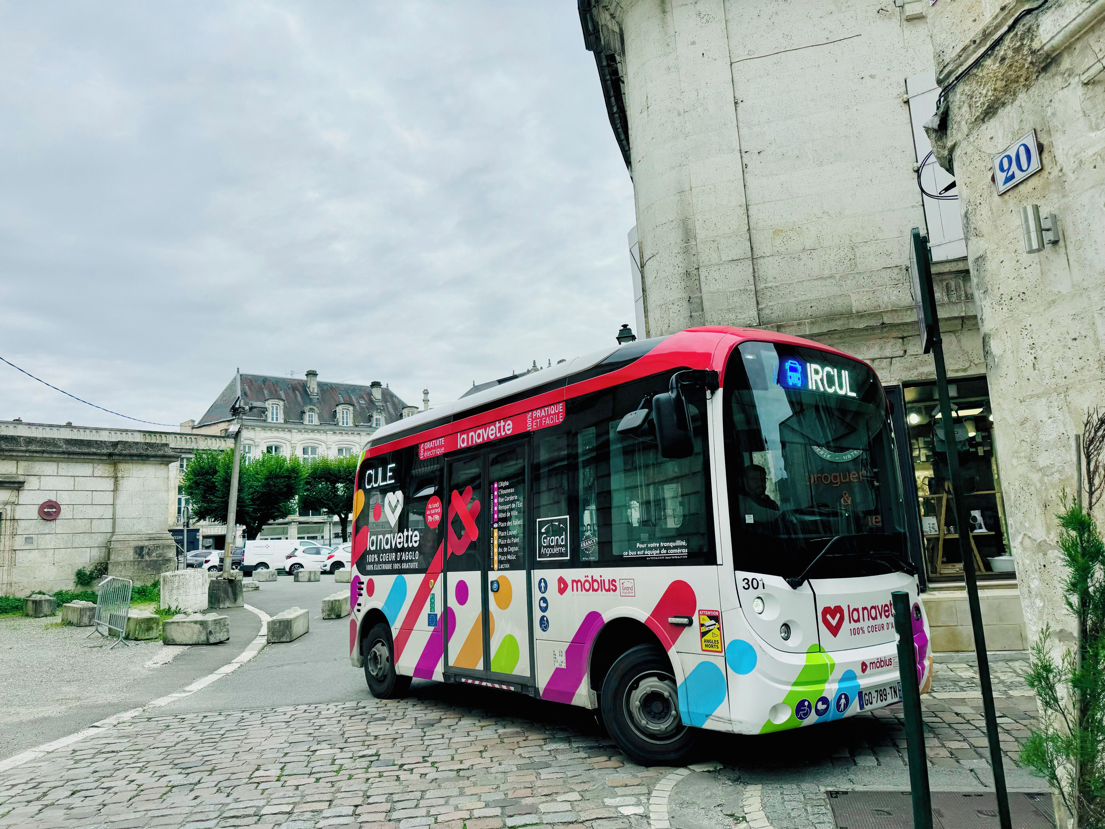 Un autobus aux couleurs vives, orné de publicités, est garé dans une rue pavée.