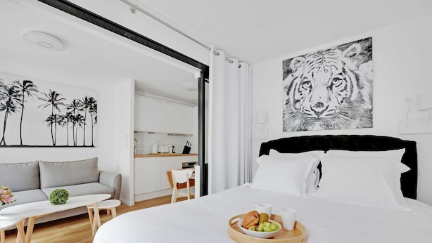 Een moderne hotelkamer met een bed, een ontbijt aan een eettafel, een bank en een keuken op de achtergrond.
