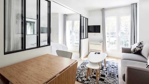 Een moderne hotelkamer met een houten bureau, een bank, een televisie en grote ramen met uitzicht op de stad.