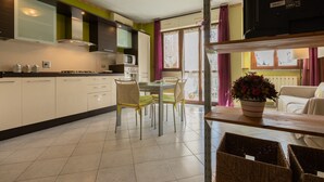 Une cuisine moderne avec des meubles blancs, une table à manger avec des chaises et un téléviseur posé sur une étagère.