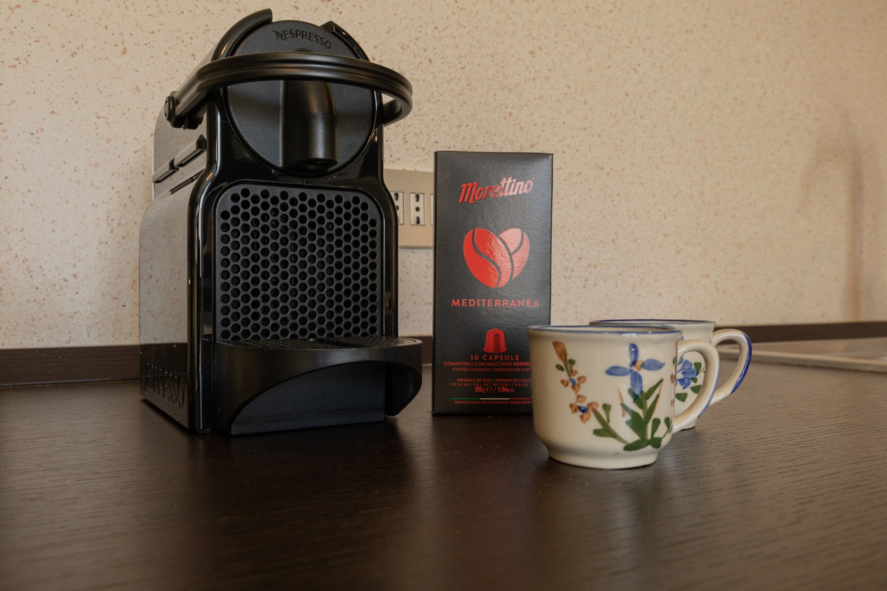 A coffee maker, a box labeled "Morettino Mediterranea," and a floral mug on a wooden table.