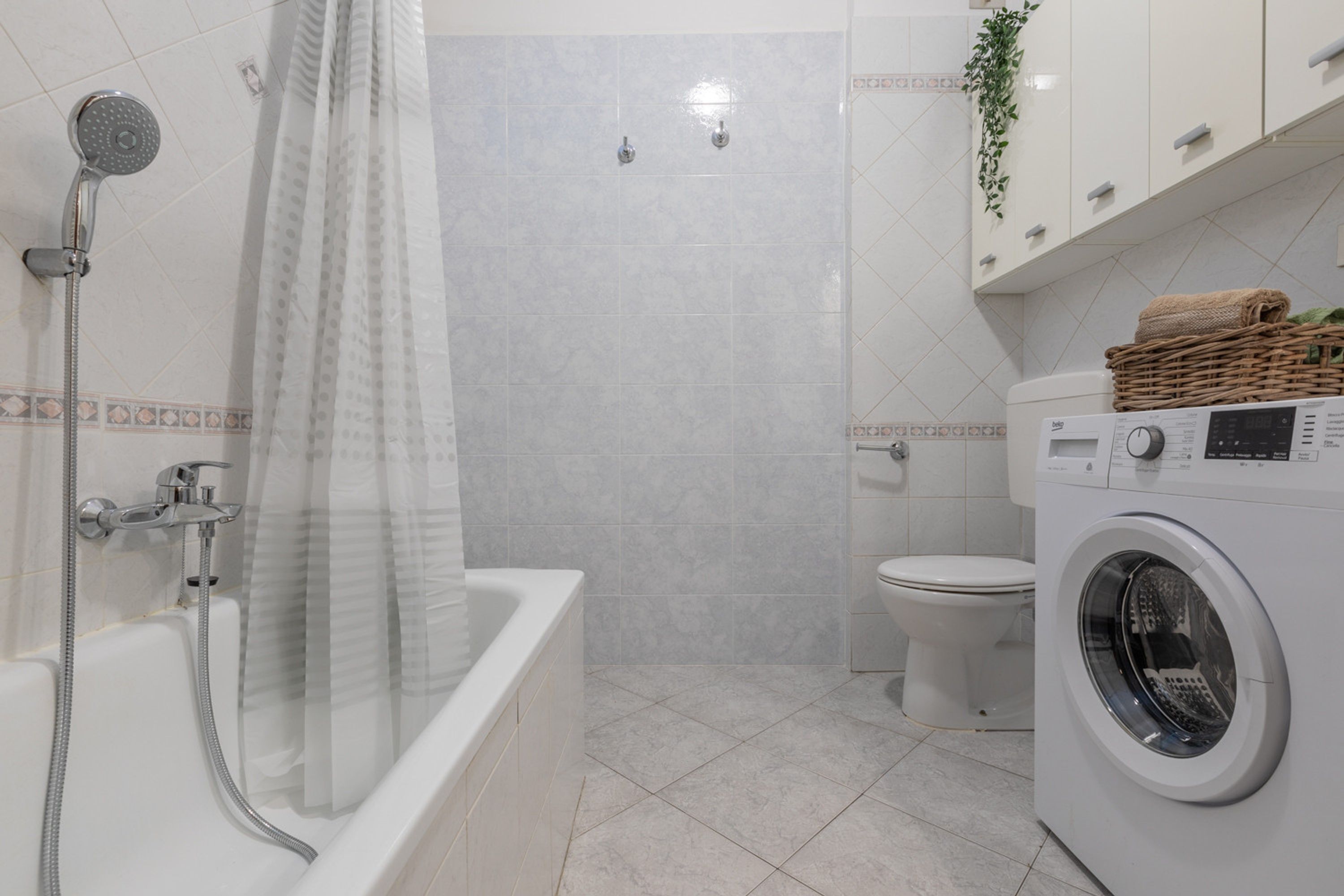 A modern bathroom with a bathtub, shower, toilet, and a washing machine.