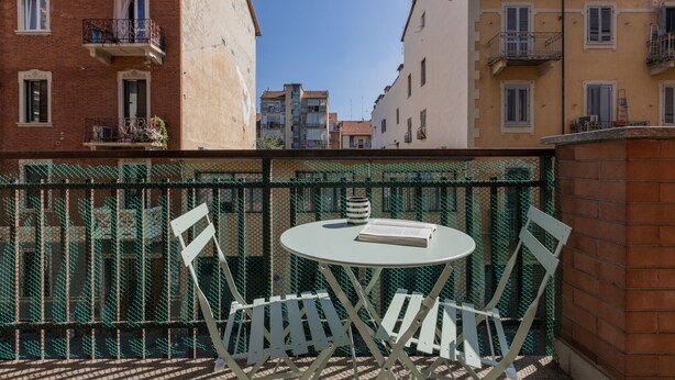 Un balcon avec une table et des chaises blanches, un livre et un vase.