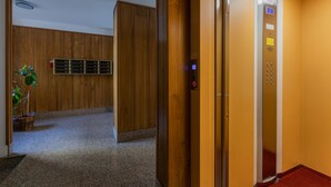 Un ascenseur doté d’un écran numérique, d’un mur en bois et d’une plante en pot dans le couloir.