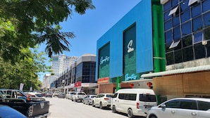 A street lined with parked cars and buildings, including a blue building with a large window and a sign that reads "Sano." - Hotel O Signature Inn Miri (Miri)