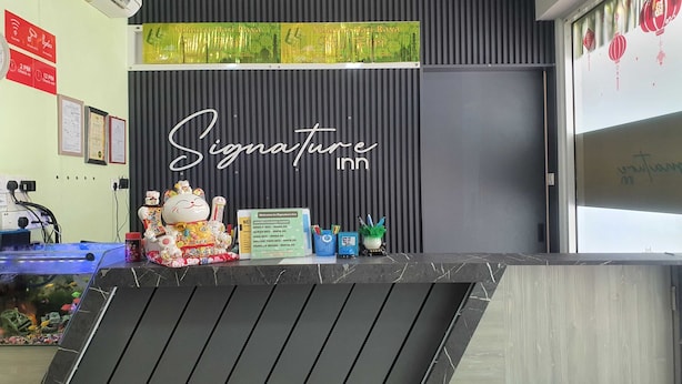 A reception desk at Signature Inn with a black and white striped wall, a neon sign, and various items like a cat figurine, a menu, and a small plant. - Hotel O Signature Inn Miri (Miri)