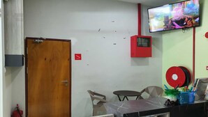 A room with a wooden door, a small table with chairs, a television mounted on the wall, and a red fire alarm box. - Hotel O Signature Inn Miri (Miri)