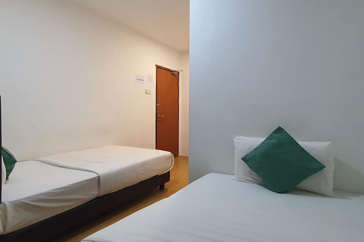A small, clean room with two single beds, a wooden floor, and a door with a sign on the wall.