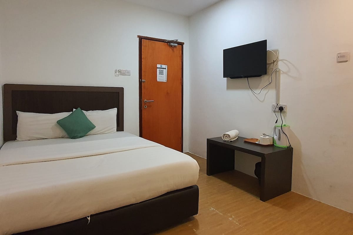 A hotel room with a bed, a desk, a television mounted on the wall, and a door.