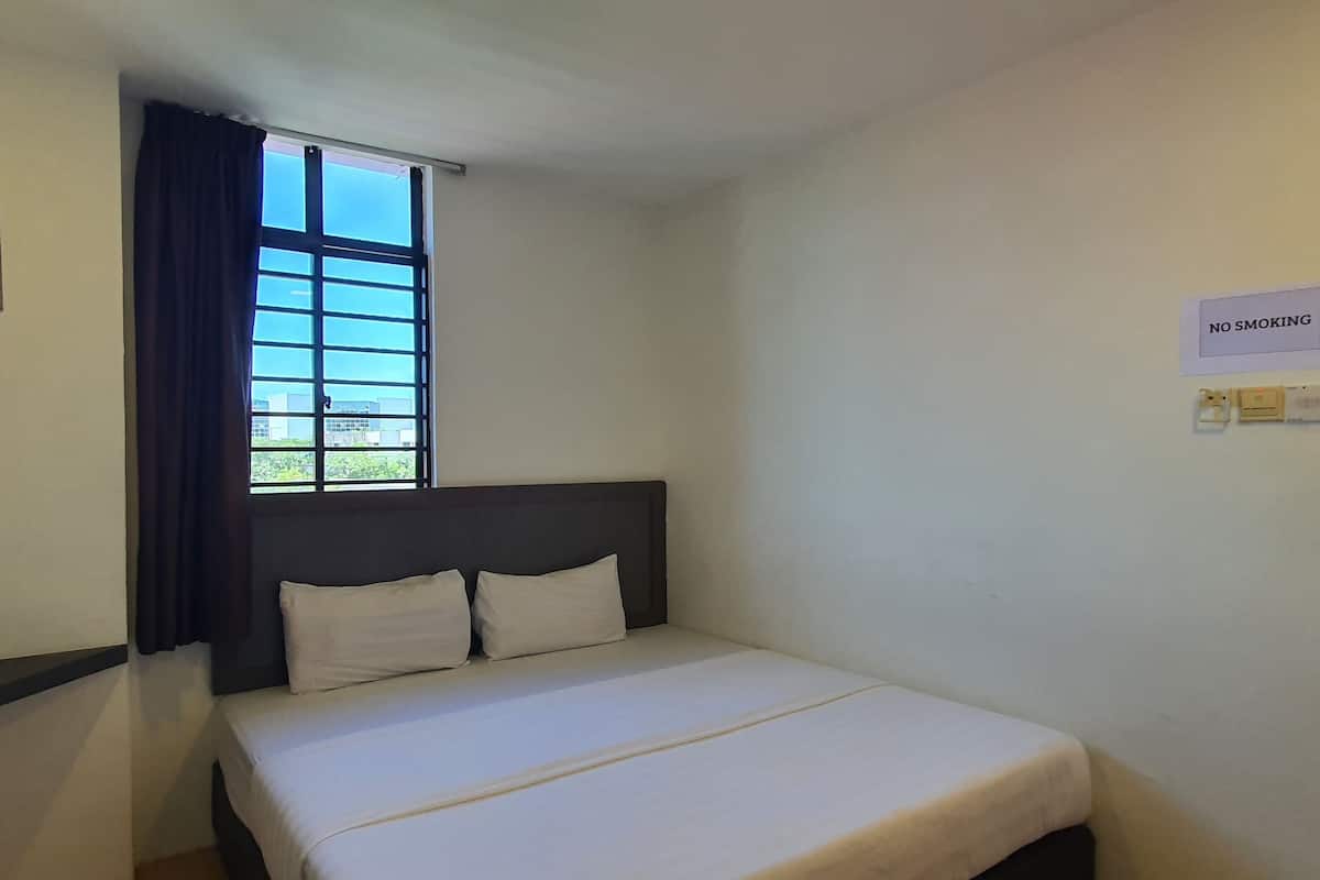 A single bed with a headboard, a window with curtains, and a 'NO SMOKING' sign on the wall.