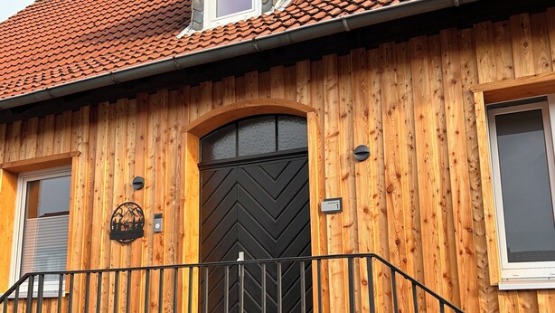 Una casa de madera con puerta negra, un letrero pequeño y una ventana.
