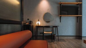 Een moderne kamer met een bank, een tafel met lamp, een stoel, een ronde spiegel en een televisie op een houten plank.