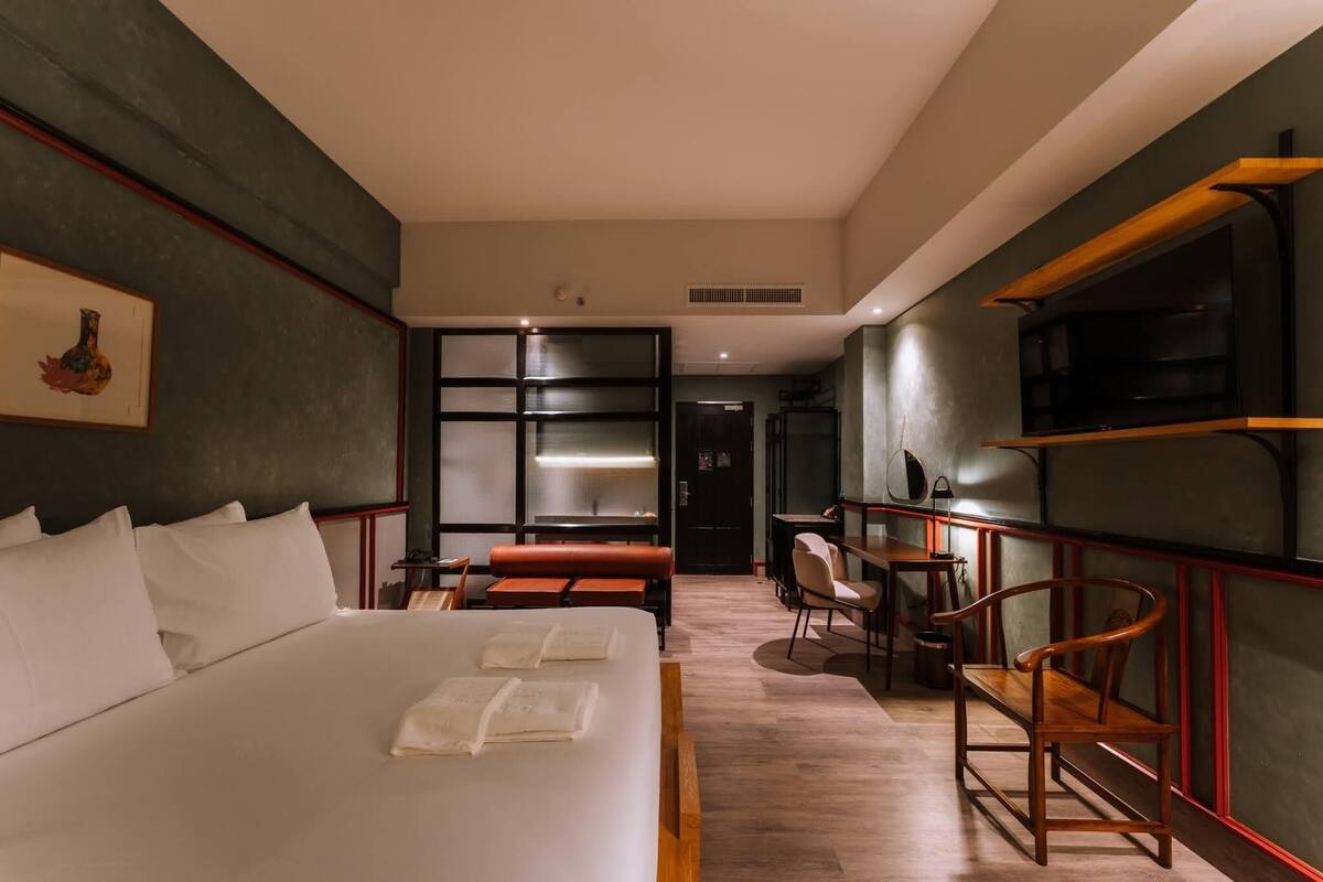 Une chambre d’hôtel moderne avec un grand lit, un bureau, une chaise et un téléviseur posé sur une étagère.
