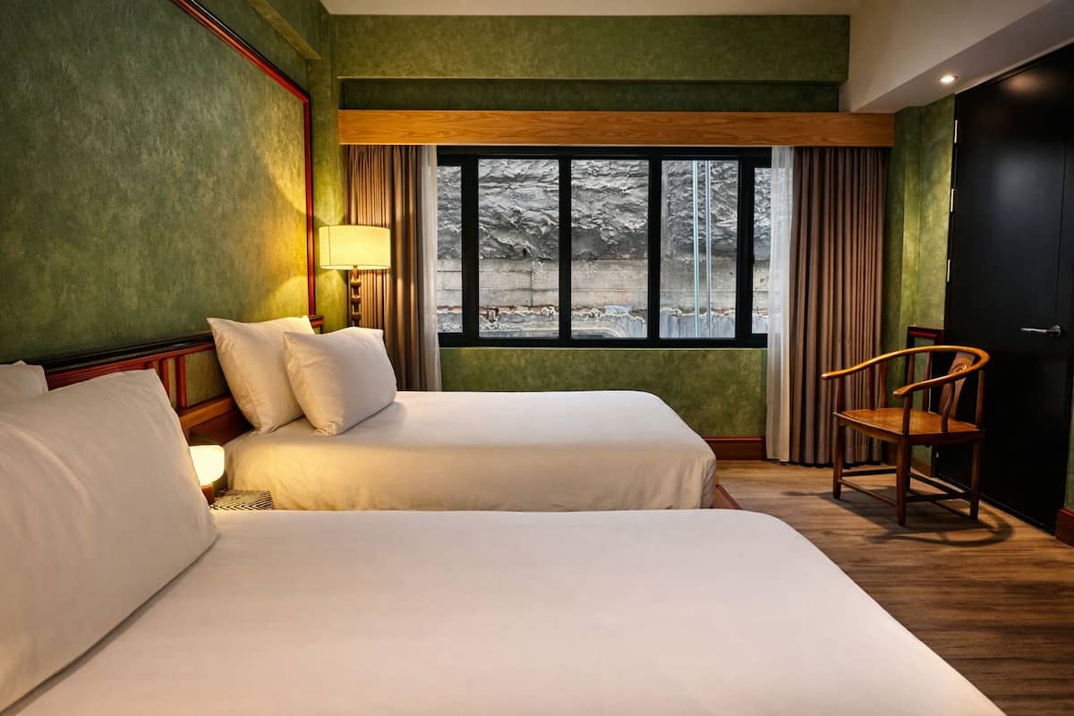 Une chambre d’hôtel avec deux lits, une chaise en bois, une fenêtre donnant sur un paysage agréable et des murs verts.