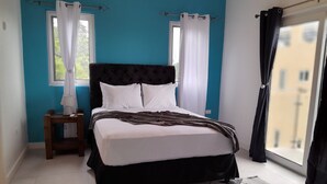 A bedroom with a bed, a nightstand, a window with curtains, and a view of buildings outside. - Kingston view (Kingston)