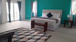 A bedroom with a large bed, a wooden bench, a patterned rug, and a view of the outside through a window. - Kingston view (Kingston)