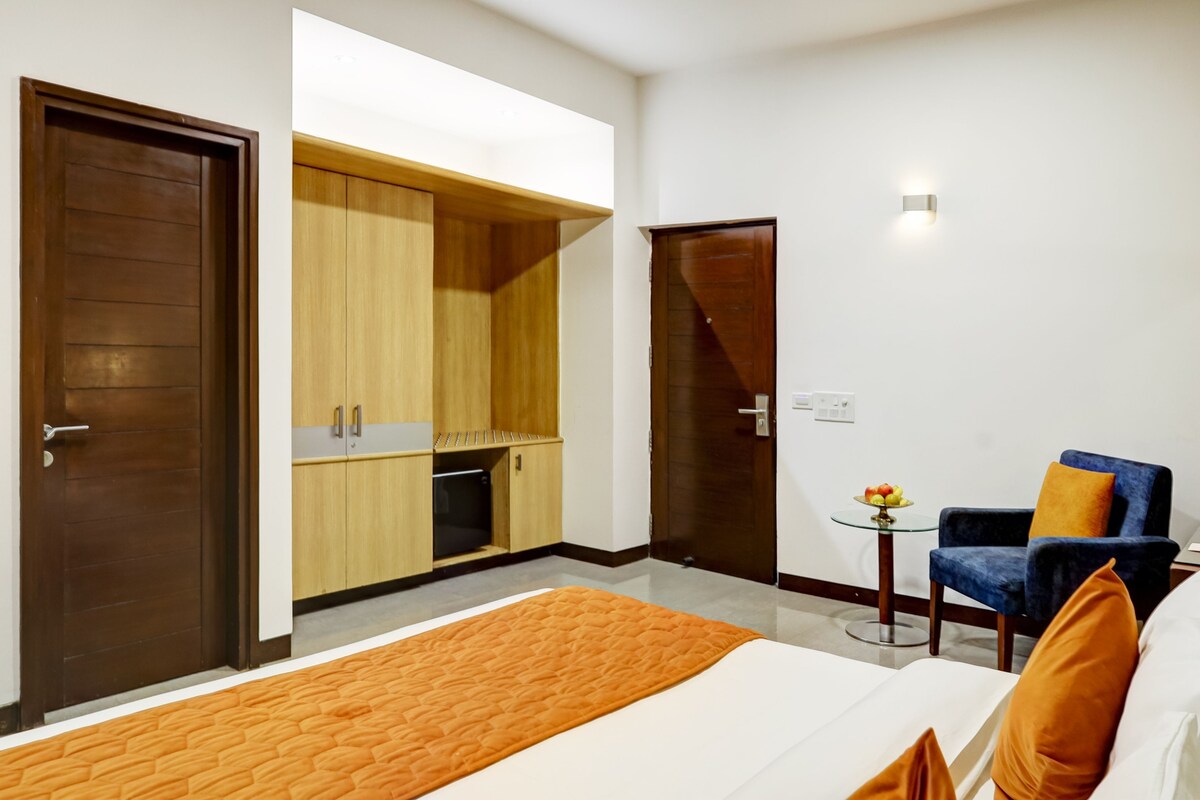 A hotel room with a bed, a seating area with a chair, a small table with fruit, and a wardrobe.