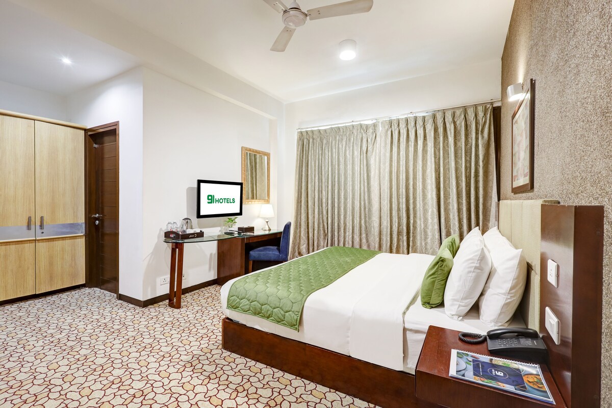 A hotel room with a bed, a desk with a computer, a TV, and a ceiling fan.