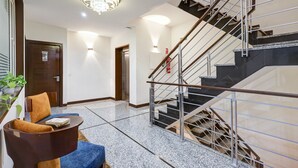 A modern lobby with a marble floor, a staircase with metal railings, and a chandelier. - Hotel 91 Golf Course Road (Gurugram)