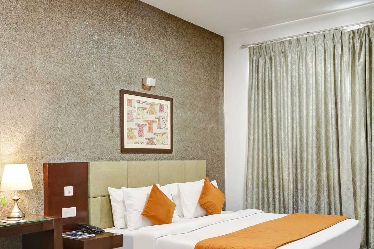 A hotel room with a bed, a desk with a lamp, a telephone, a ceiling fan, and a window with curtains.