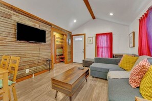 A living room with a wooden wall, a grey sofa, a wooden coffee table, and a television mounted on the wall.