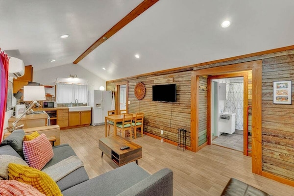 Bright open-concept living area with vaulted wood-beam ceilings, smart TV & seating for 6
