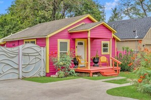 Ein rosafarbenes Haus mit Veranda, Tor und kleinem Garten.