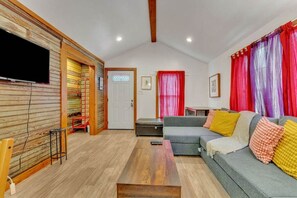 A living room with a wooden wall, a grey sofa, a wooden coffee table, and red curtains. - Pink Bungalow! (Austin)
