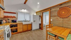 A compact kitchen with wooden cabinets, a white refrigerator, and a dining table with chairs. - Pink Bungalow! (Austin)