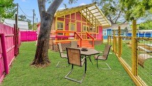 A colorful wooden playhouse with a porch and a table with chairs in a backyard. - Pink Bungalow! (Austin)