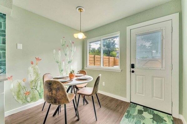 A dining area with a table set for four, chairs, a ceiling light, a window with blinds, and a door with a window.