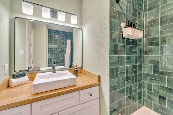 A bathroom with a white sink, a mirror, and a shower with green tiles.