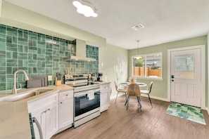 A kitchen with a green tiled backsplash, white cabinets, a stove, and a dining area with a table and chairs.
