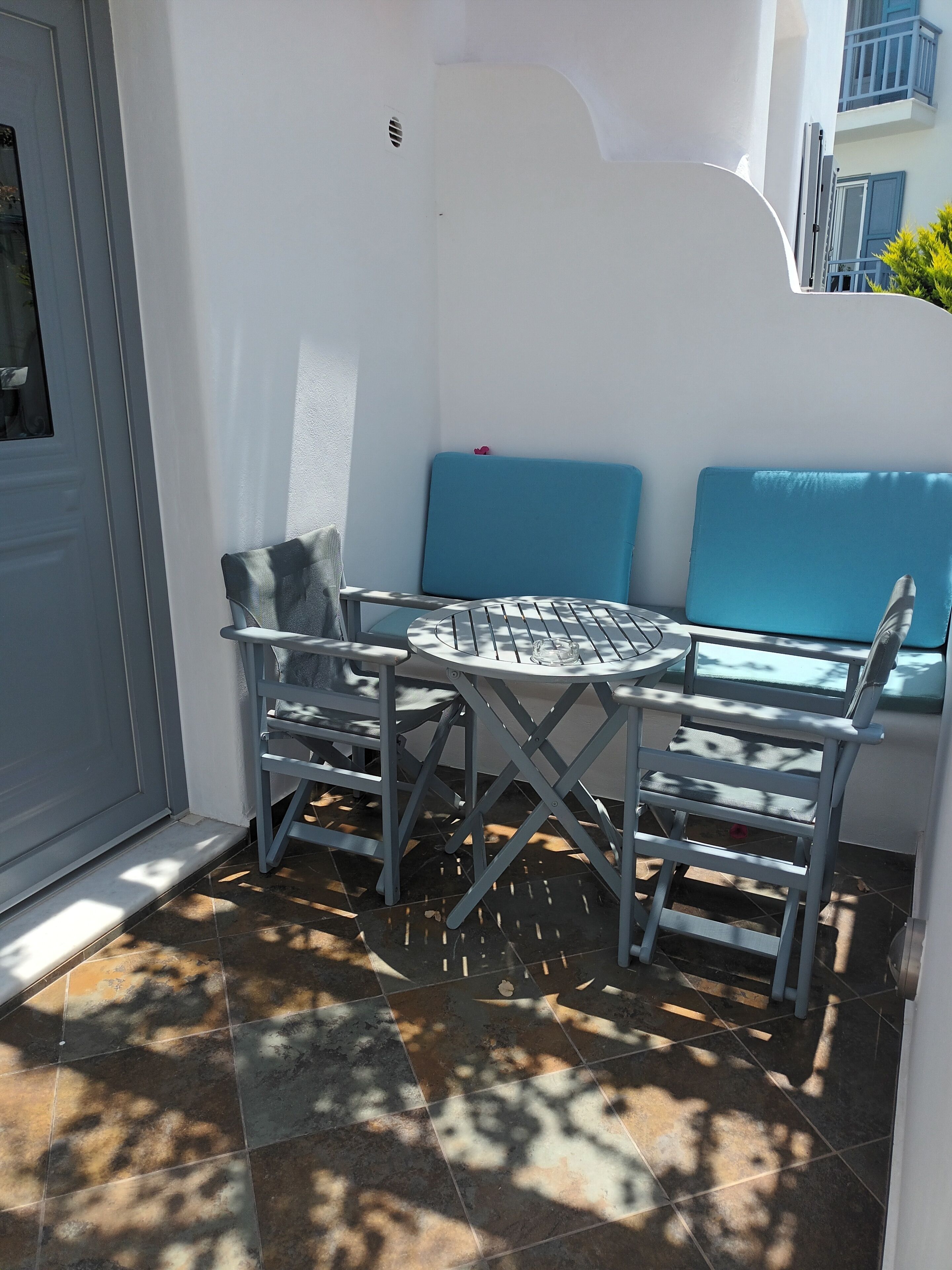 Un patio con una mesa redonda y dos sillas, un banco azul acolchado y una pared blanca.