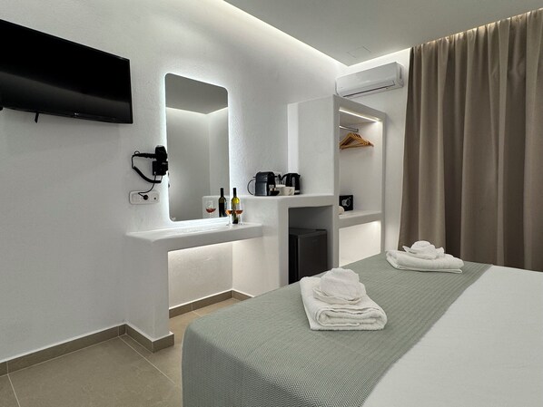 Una camera d'albergo moderna con televisione a schermo piatto, uno specchio integrato, un minibar, una macchina da caffè e un letto rifatto con asciugamani.