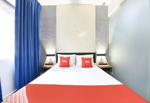 Een hotelkamer met een bed, twee nachtkastjes, een muur met een lamp en een raam met blauwe gordijnen.