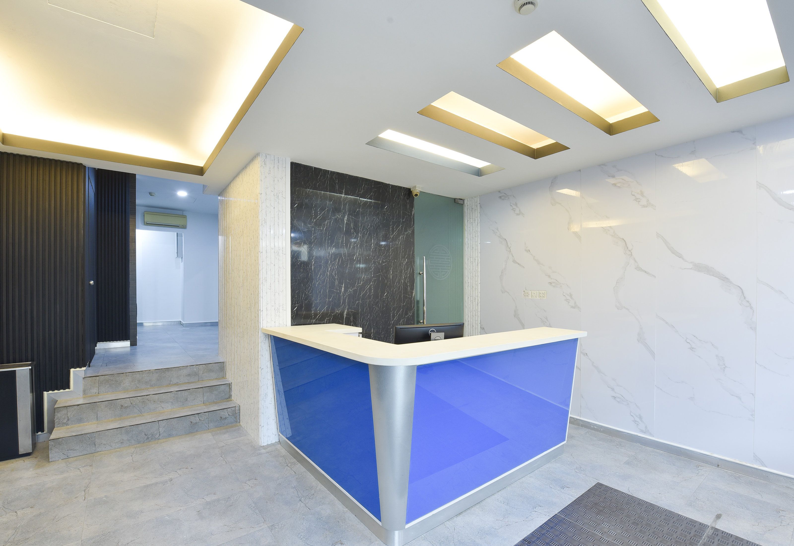 A reception area with a blue counter, marble walls, and a staircase leading to another room.