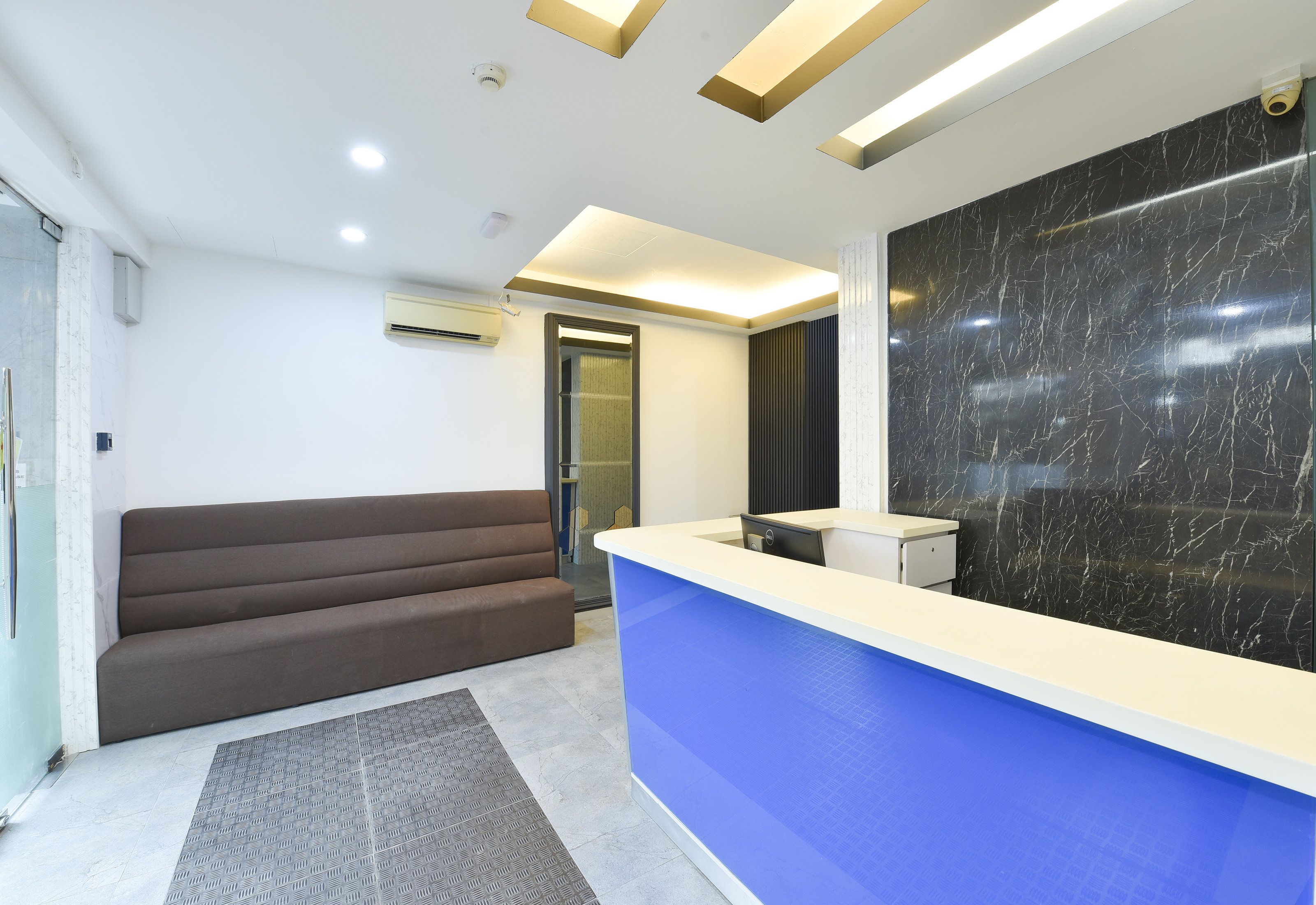 A reception area with a blue counter, a brown sofa, and a black marble wall.