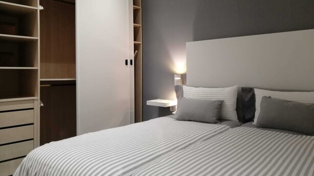 A bedroom with a bed, bedside table, lamp, and a wardrobe with open doors. - Laidatxu Beach Apartment in Mundaka (Mundaka)