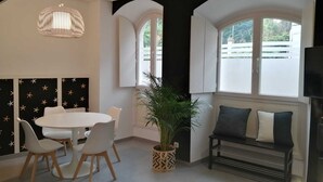 A modern living room with a round dining table, white chairs, a black and white patterned wall, a large potted plant, a black bench with cushions, and a TV on a stand. - Laidatxu Beach Apartment in Mundaka (Mundaka)