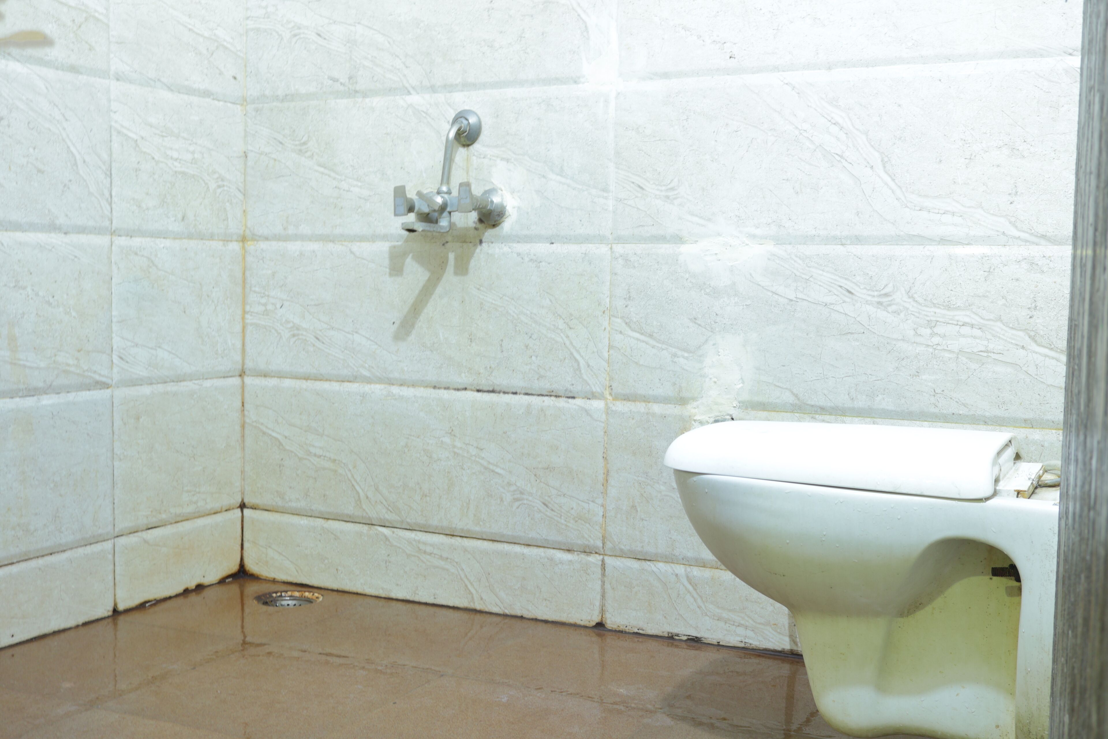 Ein Badezimmer mit weißen Fliesen, einer weißen Toilette und einer Duscharmatur.