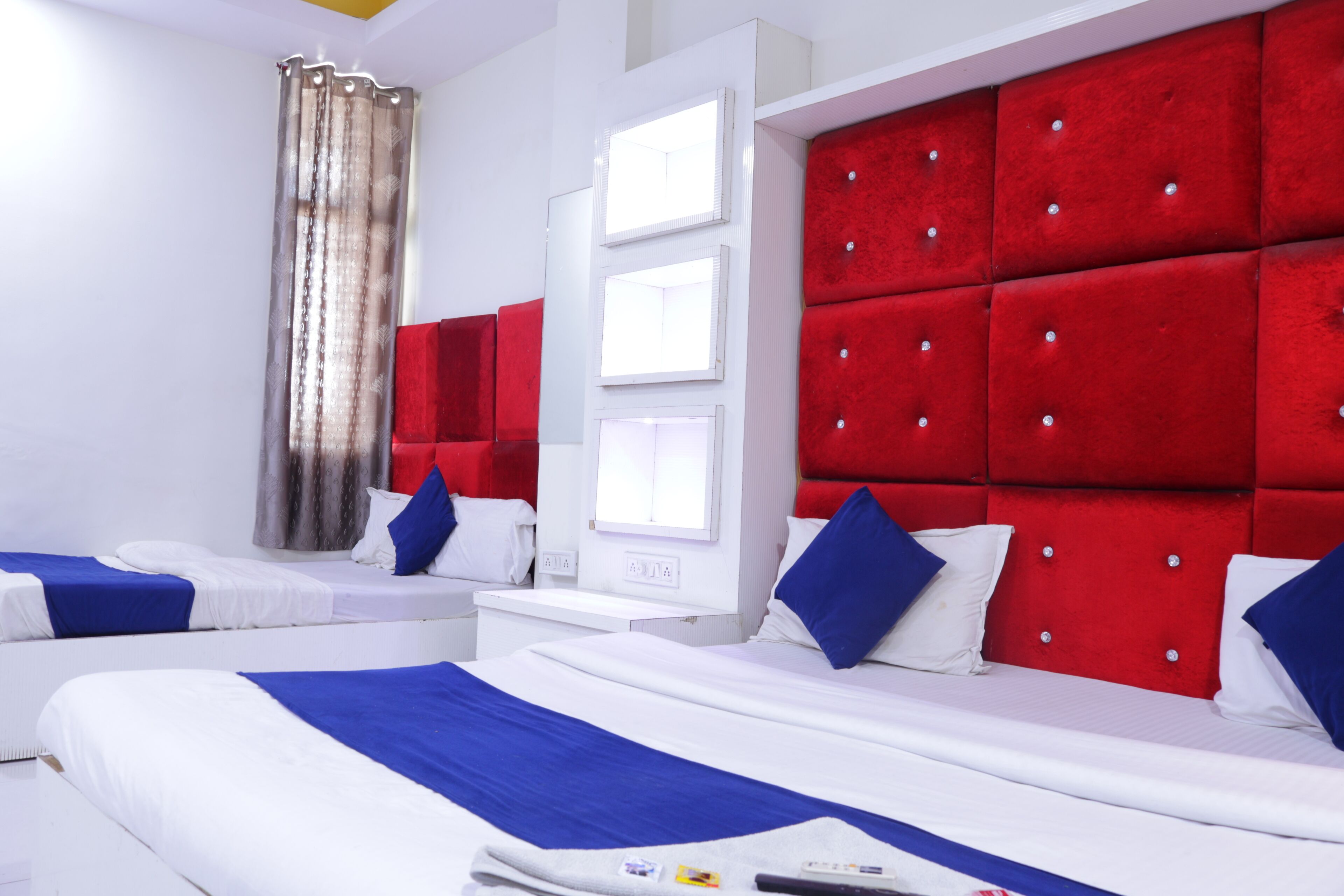 A hotel room with two beds, red upholstered headboards, white walls, and a window with curtains.