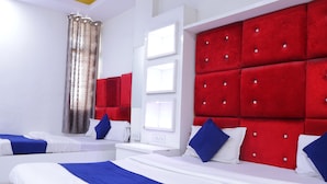Ein Hotelzimmer mit zwei Betten, roten Polsterkopfteilen, weißen Wänden und einem Fenster mit Vorhängen.