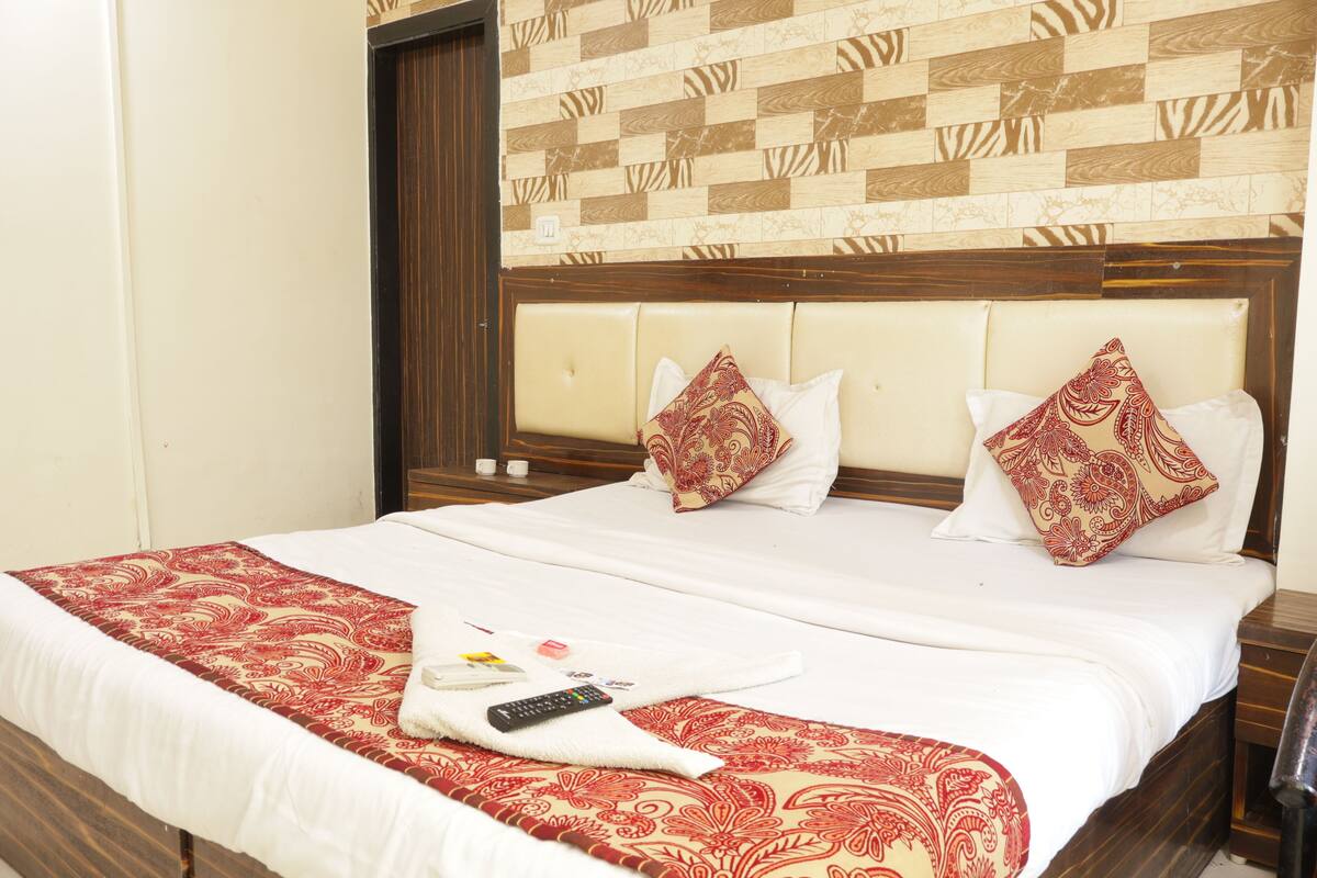 A hotel room with a large bed, two pillows, a blanket, and a remote control.