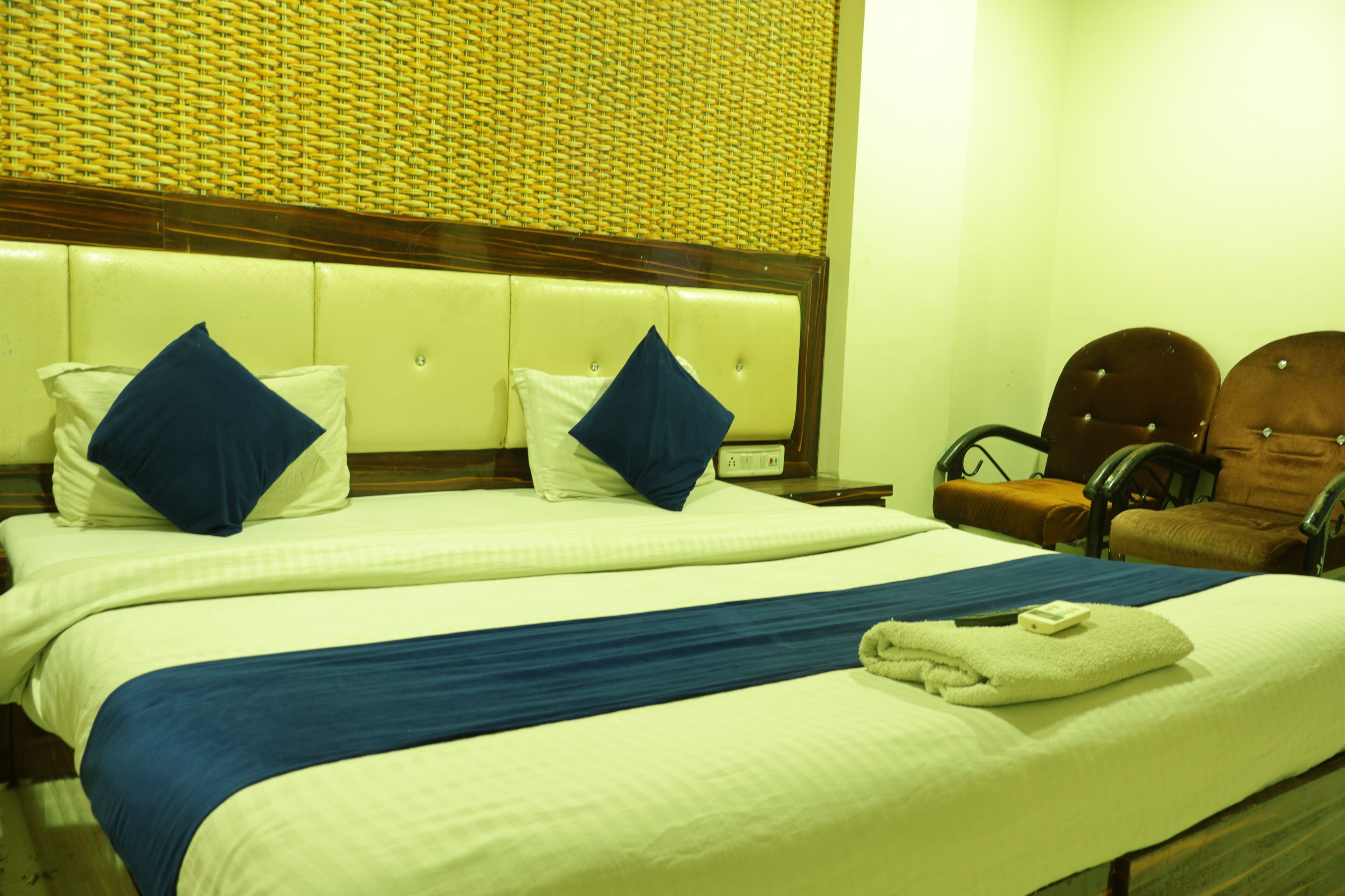 A hotel room with a large bed, two nightstands, a chair, and a headboard with a woven pattern.