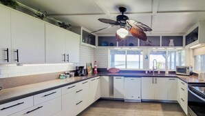A modern kitchen with white cabinets, a wooden countertop, a built-in dishwasher, and a ceiling fan.