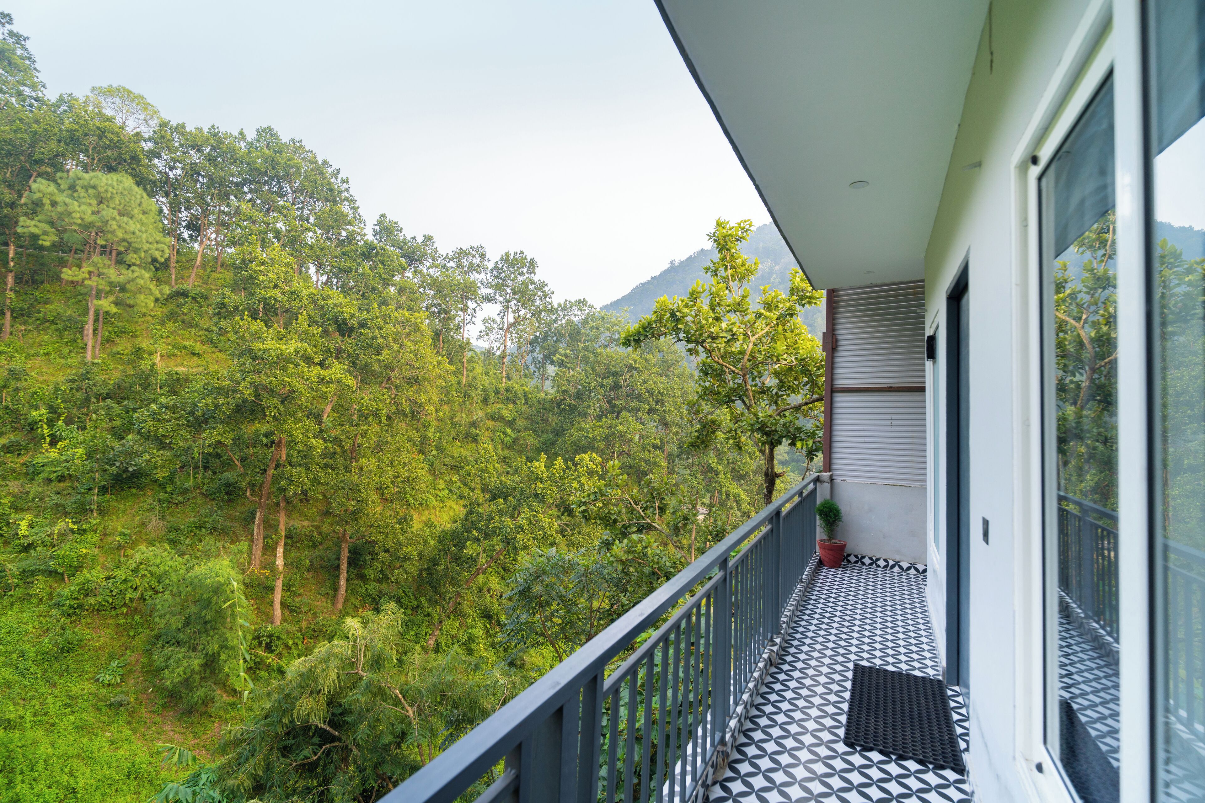 Een balkon met een zwart-wit patroon vloer, met uitzicht op een weelderig groen bos en een berg in de verte.