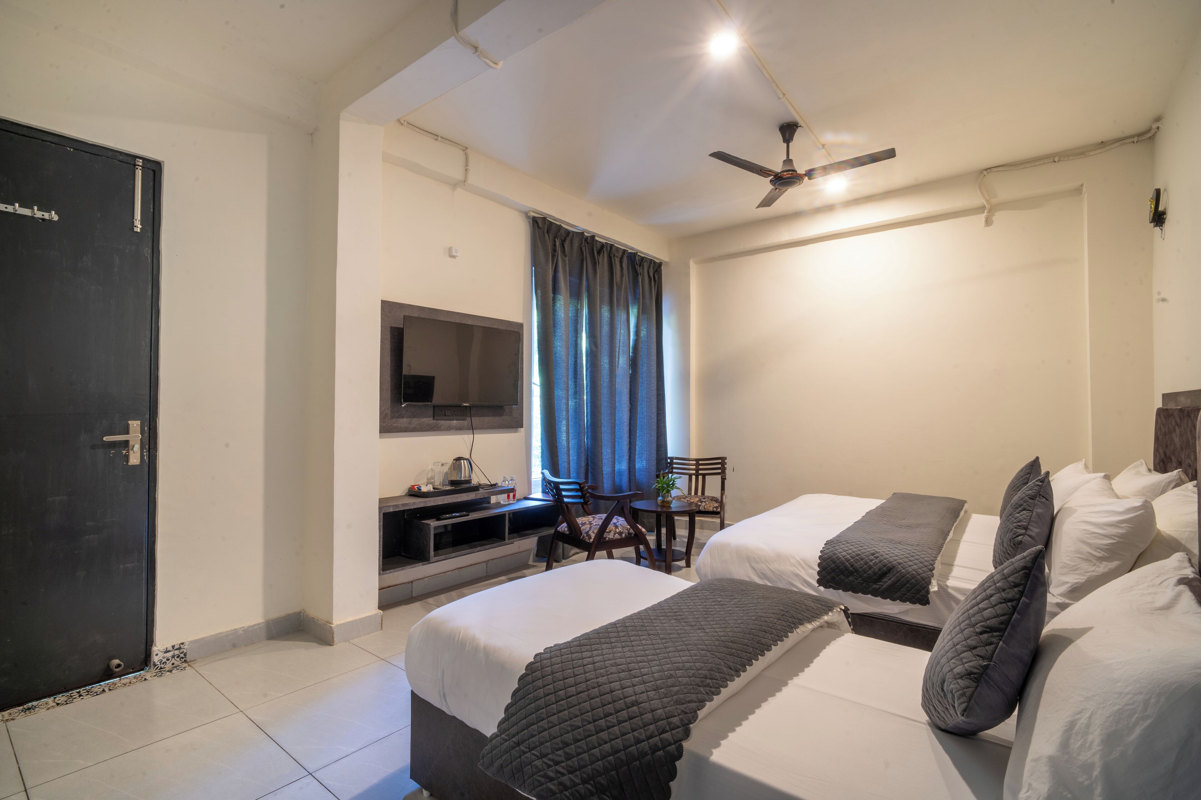 A hotel room with two beds, a TV, a desk, and a ceiling fan.