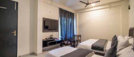 A hotel room with two beds, a TV, a desk, and a ceiling fan.